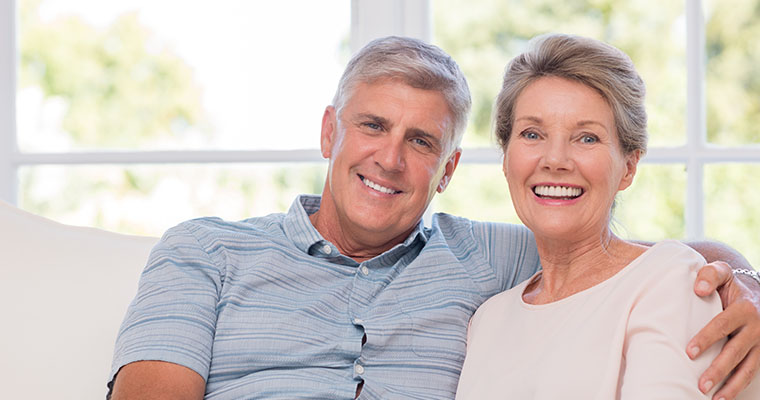 A mature couple is sitting on a sofa, smiling